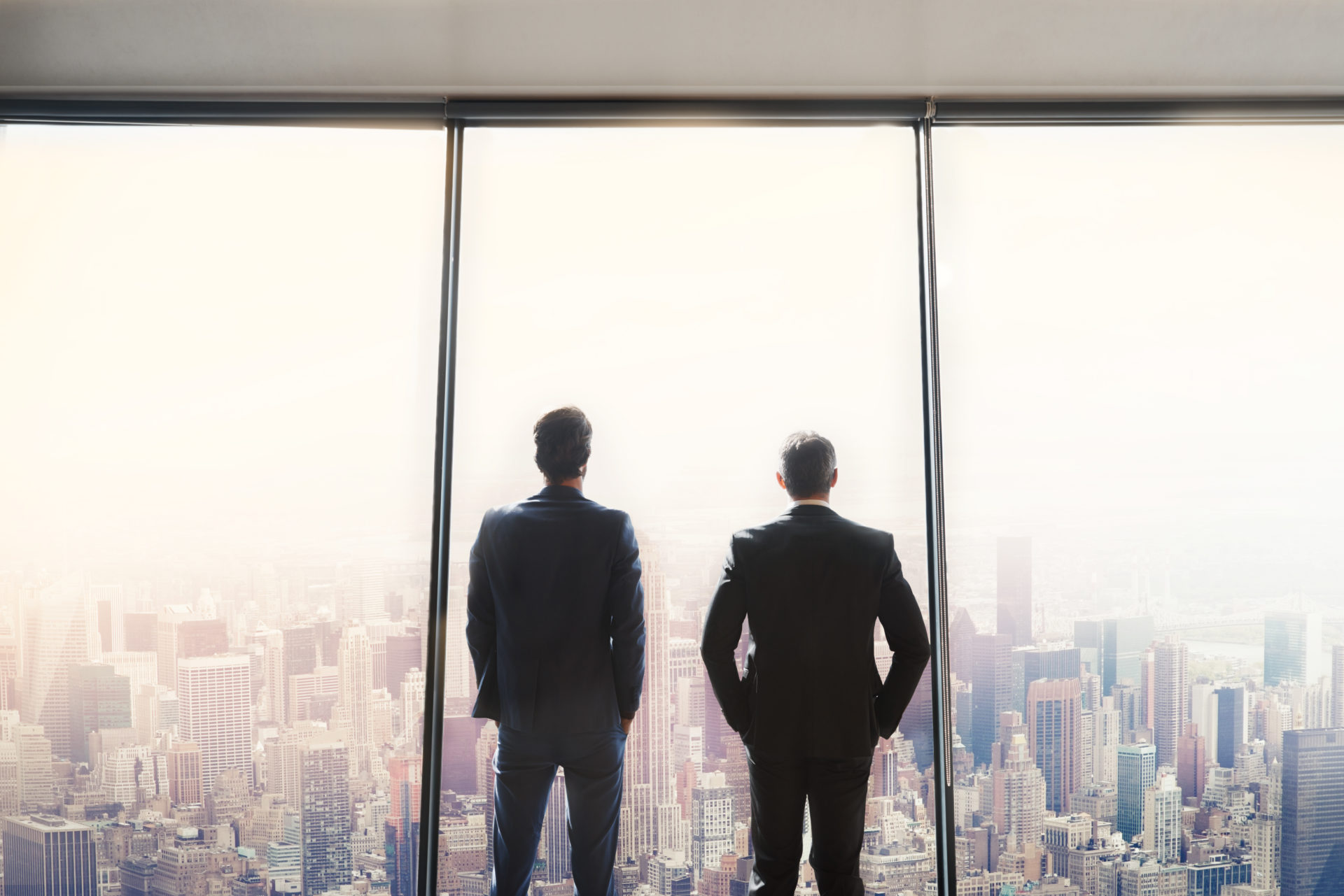 Rearview shot of two corporate businessmen looking out from a large window in their office