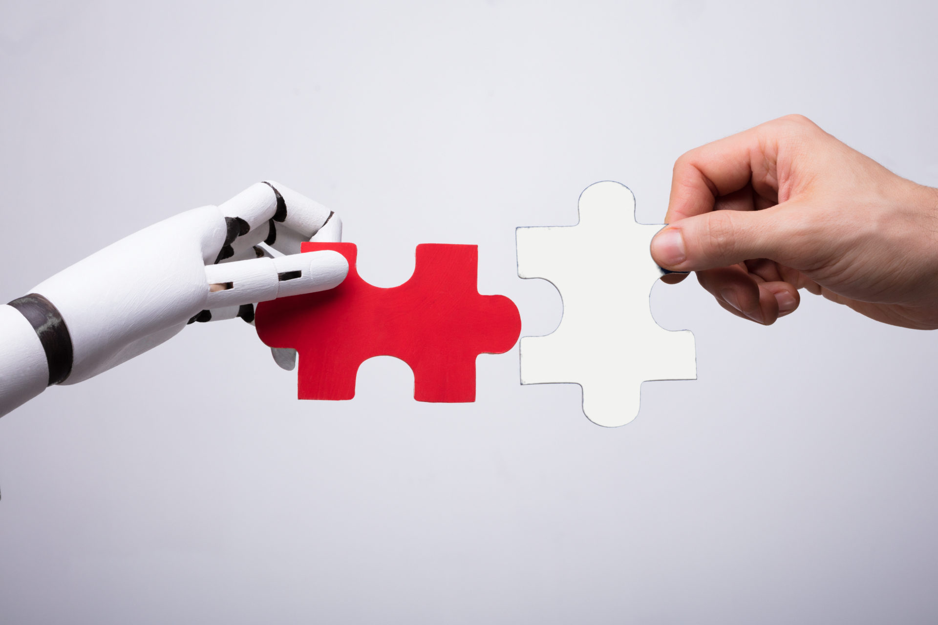 Close-up Of Robot And Human Hand Holding Red And Blue Jigsaw Puzzle