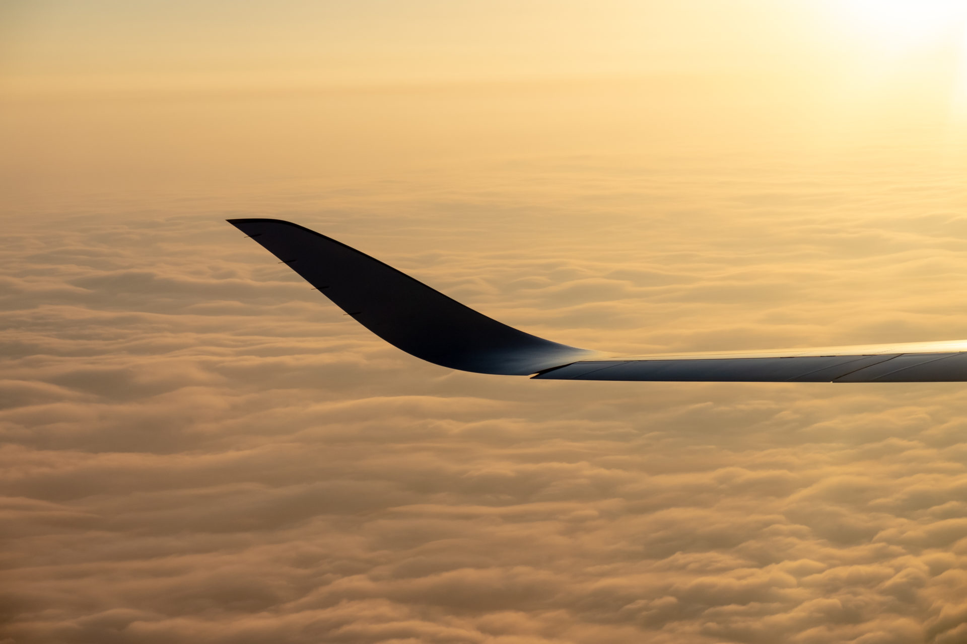 Airplane winglet over cloud carpet at sunset